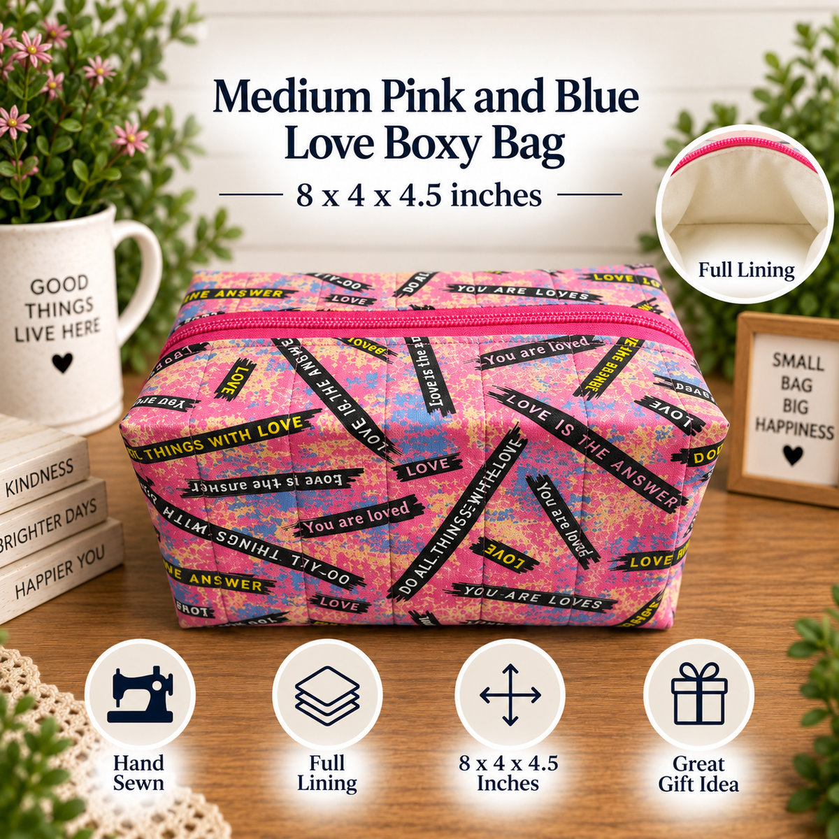 A pink and blue patterned fabric boxy bag with a pink zipper, displayed on a wooden surface with decorative props including a mug, flowers, and small boxes. Text at the top reads 'Medium Pink and Blue Love Boxy Bag' with dimensions, and circular icons at the bottom highlight features like hand sewing, full lining, size, and gift suitability.