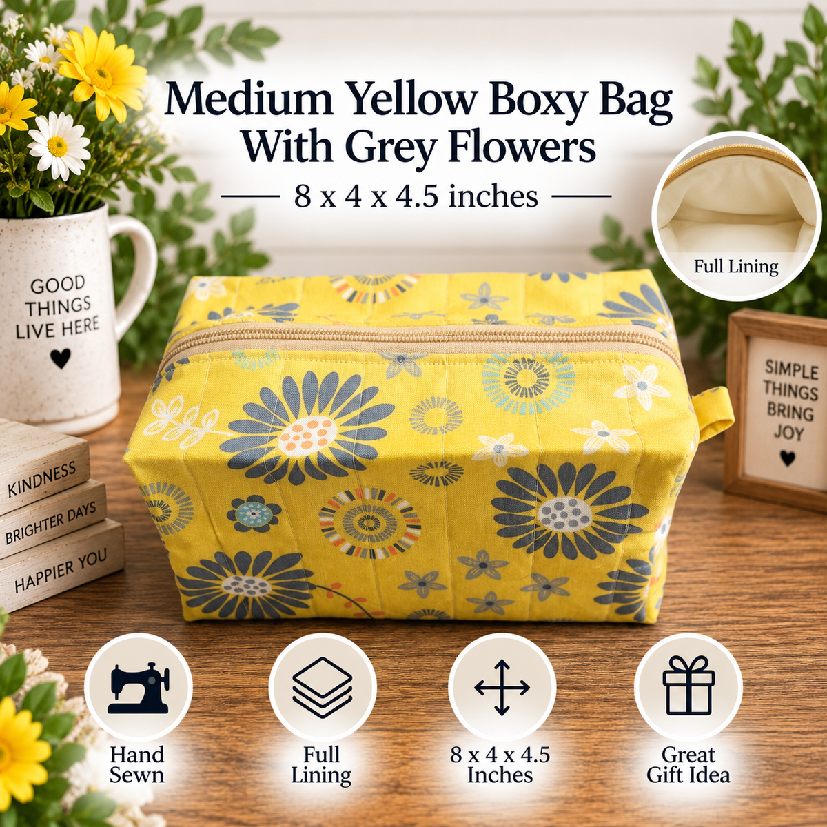 A yellow fabric boxy bag with a blue and grey floral pattern, shown on a wooden table with decorative props including flowers, a mug, and small signs. Text on the image reads 'Medium Yellow Boxy Bag With Grey Flowers' and includes feature icons for hand sewn, full lining, dimensions, and gift idea.