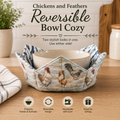 A fabric reversible bowl cozy with a rooster print, shown holding a ceramic bowl on a wooden countertop. Text at the top reads 'Chickens and Feathers Reversible Bowl Cozy' and there are feature icons along the bottom.