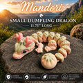 A small Mandori dumpling dragon toy arranged on a large rock outdoors, with mountains and a sunset in the background. Text at the top reads 'Mandori Small Dumpling Dragon 11.