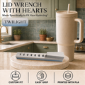 A beige HydroJug travel tumbler with a straw stands on a kitchen counter next to a gray and beige lid wrench tool labeled 'TWILIGHT.' The background shows a green kitchen interior.