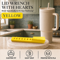 A yellow lid wrench with heart-shaped teeth is displayed on a round stone coaster in a kitchen setting, next to a beige HydroJug tumbler. The image includes text overlays describing the product and features, and three icons at the bottom highlighting its custom fit, easy grip, and PLA printed material.