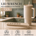 A tan lid wrench tool for HydroJug tumblers is shown on a kitchen counter next to a matching beige HydroJug tumbler with a straw. The image includes text reading 'LID WRENCH', 'Made Specifically to Fit Your HydroJug', 'TAN', and feature icons for 'CUSTOM FIT', 'EASY GRIP', and 'PRINTED WITH PLA'.
