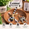 A 3D-printed Lemur keychain displayed on a wooden tray next to keys, with decorative props including a potted plant and a framed sign in the background. Text overlays read 'Lemur Keychain' and feature product selling points.