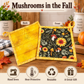 Two reusable potholders displayed on a wooden table with autumn-themed props. One side shows a yellow fabric back with small printed motifs, and the other shows a black front panel decorated with yellow sunflowers, red mushrooms, and green leaves, all with yellow borders.