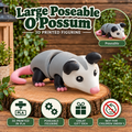A large poseable 3D-printed opossum figurine shown on a wooden stump with decorative foliage and text overlays. The opossum has a gray body, black ears and legs, and pink tail and feet.
