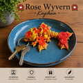 A decorative keychain shaped like a rose wyvern, shown resting on a blue ceramic plate with two keys. The keychain features yellow and orange rose-shaped scales and wings.