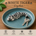 A 3D-printed white tiger keychain with black stripes and yellow eyes, shown resting on a round teal ceramic dish with keys attached. The image includes text reading 'WHITE TIGER Keychain' and feature icons at the bottom.
